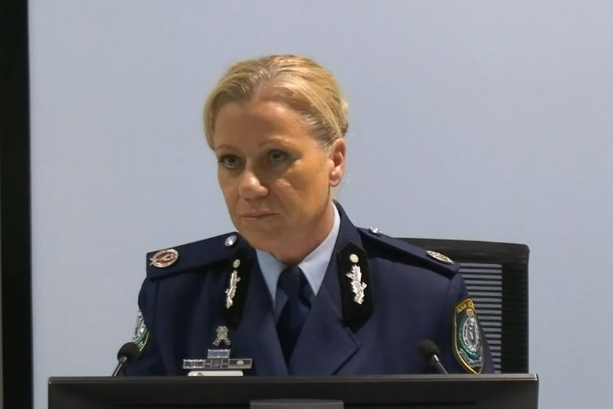 A blonde woman in police uniform sittingbehind a microphone