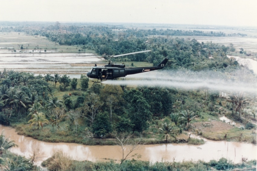 A helicopter spraying Agent Orange over vegetation.