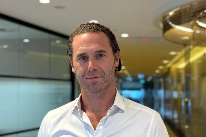 Man in white collard shirt looks at camera in office space