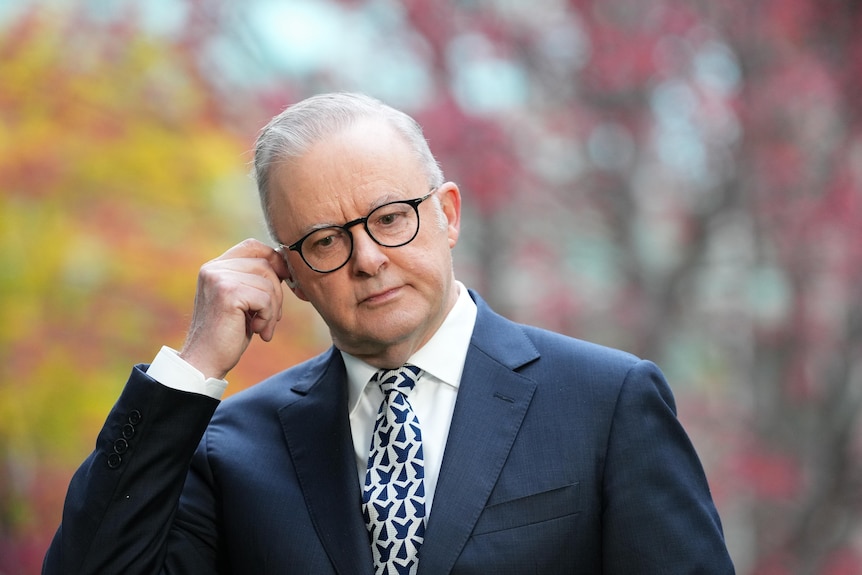 Albanese looking down in a suit while touching his ear.
