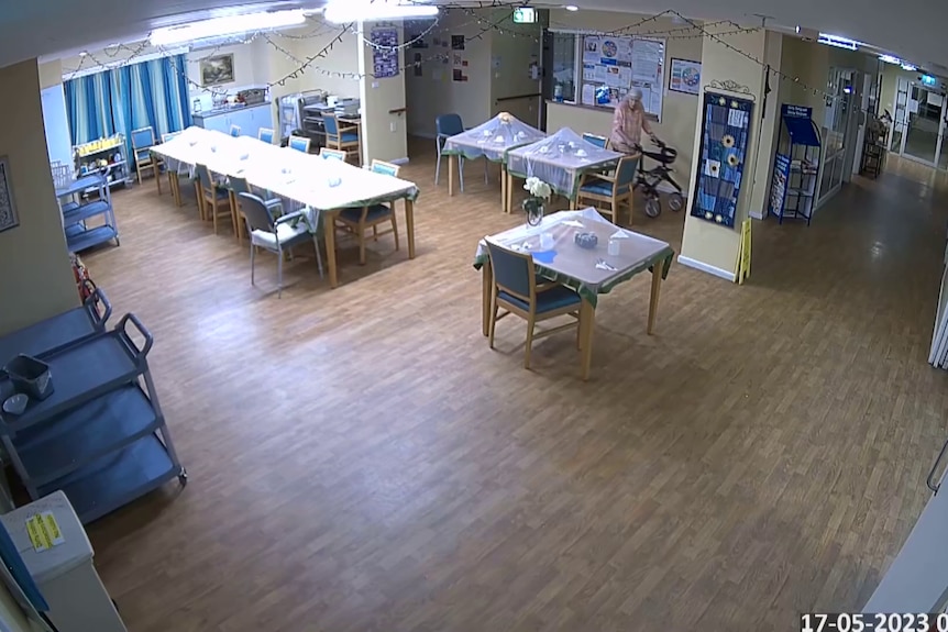 A birds eye view from the corner of a large dining room. It is empty apart from an elderly lady with a walking frame.