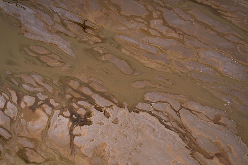 A birds-eye view of sand with brown water criss-crossing