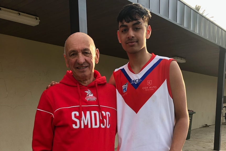 A father and his teenage son stand next to each other smiling.