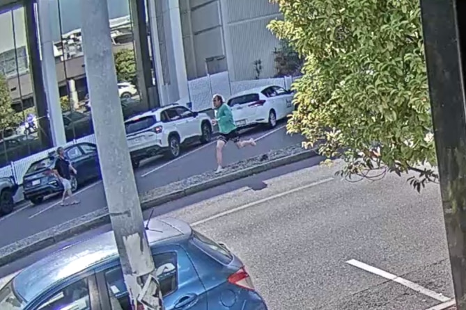 A man in a green top running across a road, away from a court building, in a CBD.