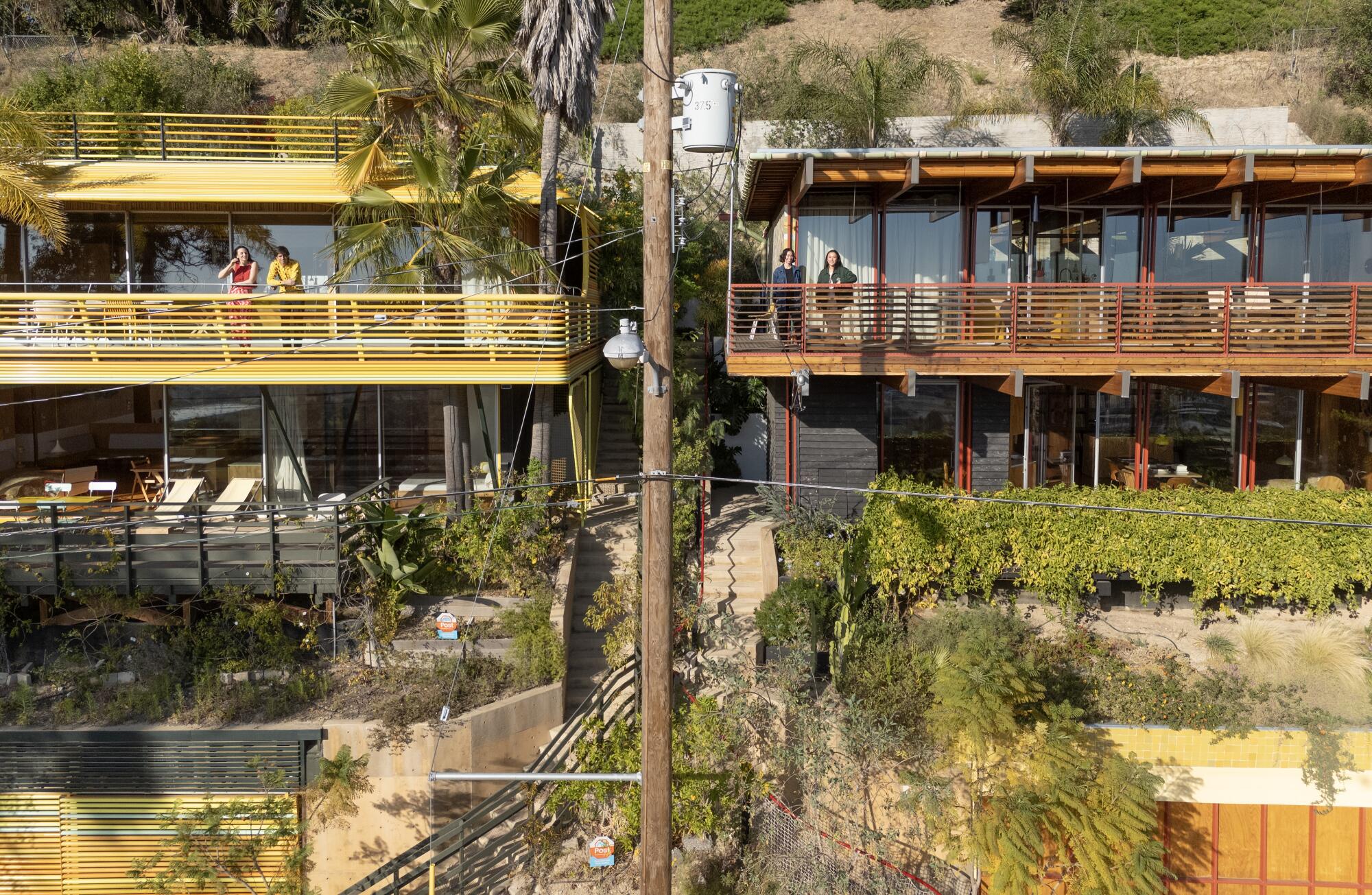 Two couples stand on their decks in side-by-side hillside homes 
