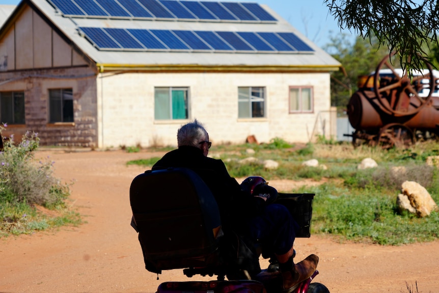 a shadow of a man driving a red gopher with a large brick shed in the background