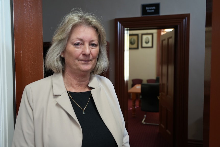 Middle aged woman with short blonde and grey bob looking serious inside council building.