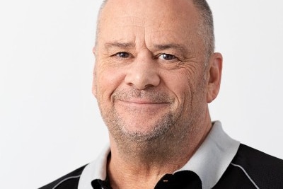 Headshot of a middle-aged man smiling. He is wearing a black top with a white collar.