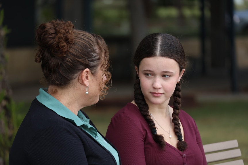 An woman with hair tied up looking at younger woman with plated piggy tails.