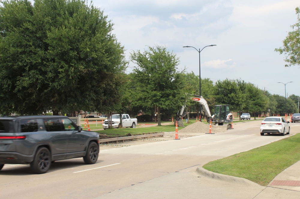 A gray SUV drives past a section of road under construction