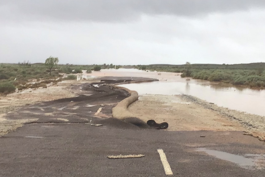 A bitumen road with water over it, and parts of the bitumen rolled up like a carpet