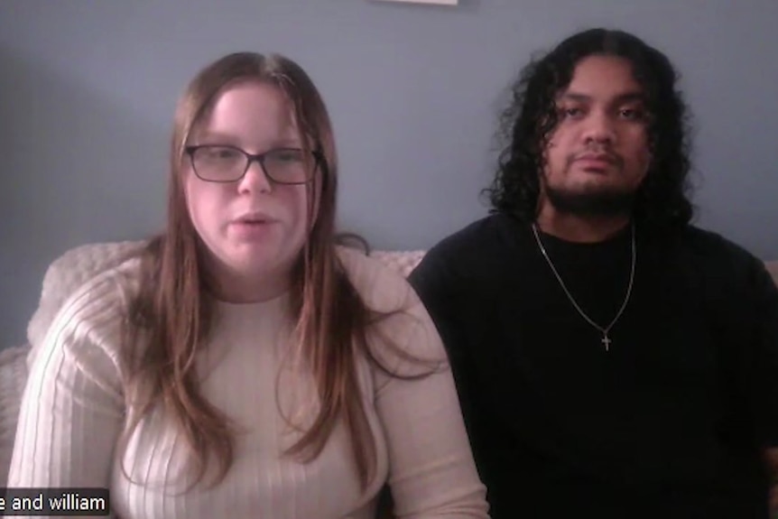 A female and male sitting on a couch looking at camera