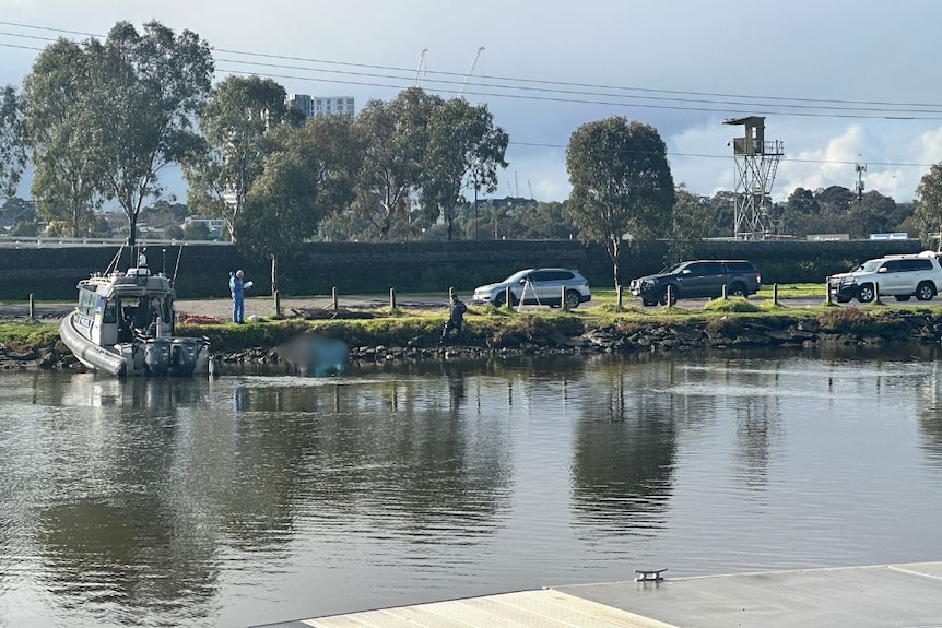 Police investigators, cars and a boat on the shore of Maribyrnong River in Flemington, Melbourne