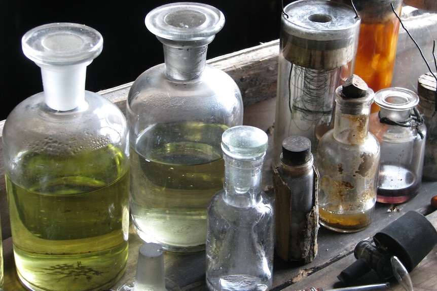 An array of old bottles with green liquid and other scientific equipment on a table.