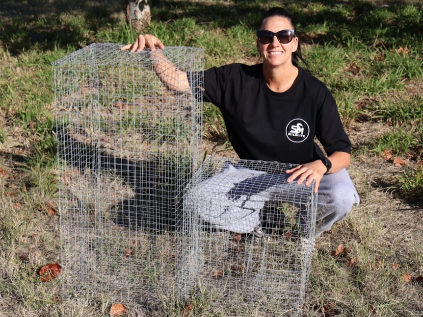 Shannon squatting behind two cages.