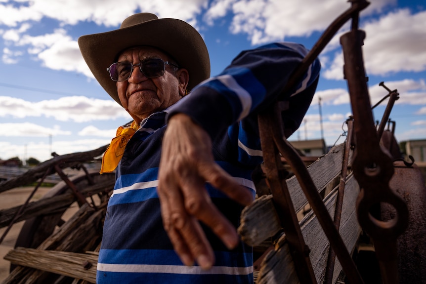 A man in a wide brim hat leans on a wooden cart