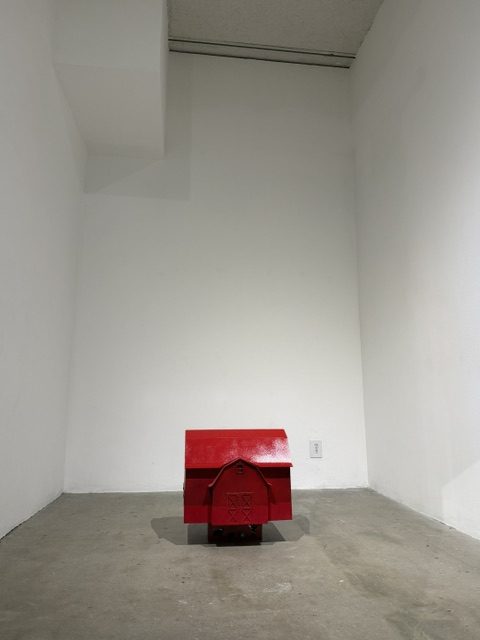 Small red house sculpture exploring themes of shelter, memory, and monumentality in the Heavy Metal exhibition.
