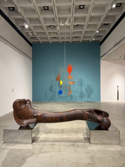 Monumental sculptural installation combining organic wood forms and colorful suspended elements at Heavy Metal in LAMAG.