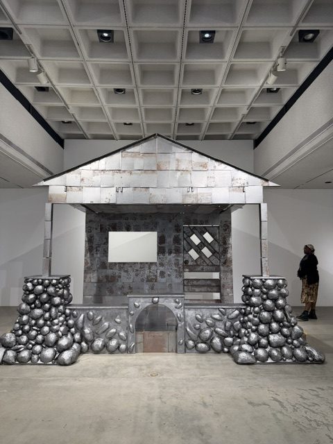 Large house-shaped sculpture constructed from metal and industrial materials displayed at Barnsdall Art Park.