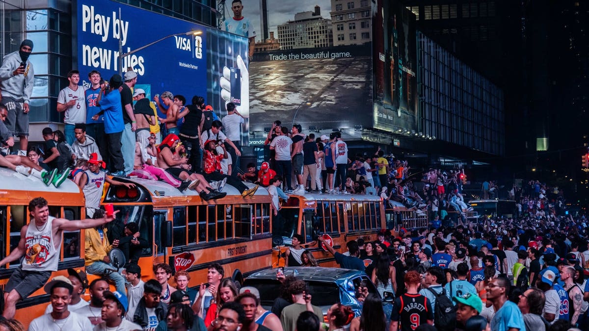 New York Knicks fans climb on buses as they celebrate after they win the NBA Finals in Times Square on June 14, 2026 in New York City.
