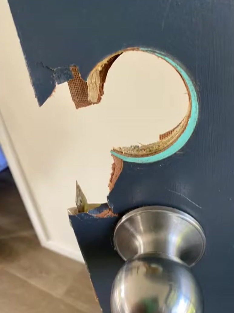 A section of a blue wooden door is missing where a lock once was installed above a silver handle.