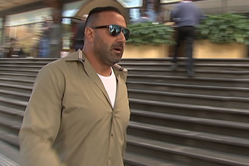 Man in sunglasses and khaki shirt with stairs in the background