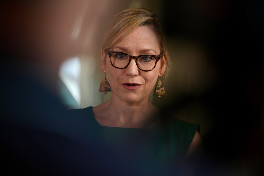 Larissa with glasses, seen past blurry figures.