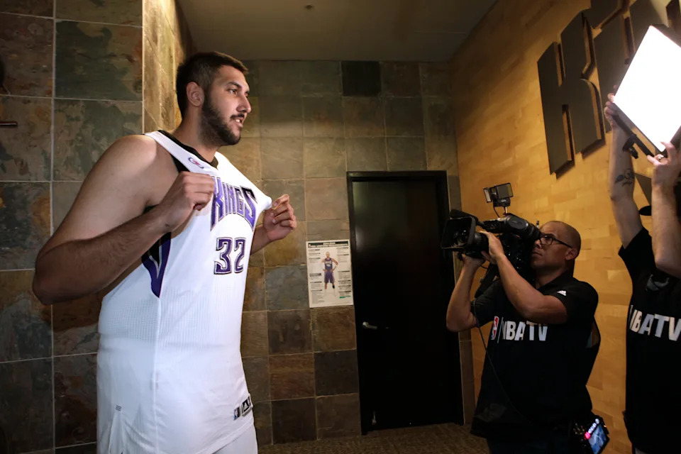 Basketball player in uniform being filmed by media crew in a hallway