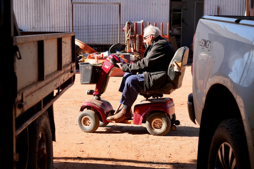 a man in blue pants, black jacket and sunglasses driving a red gopher between two vehicles