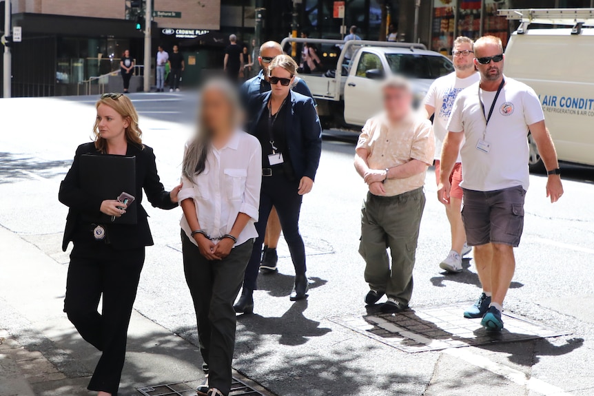 A man and a woman being led by police officers in a street.