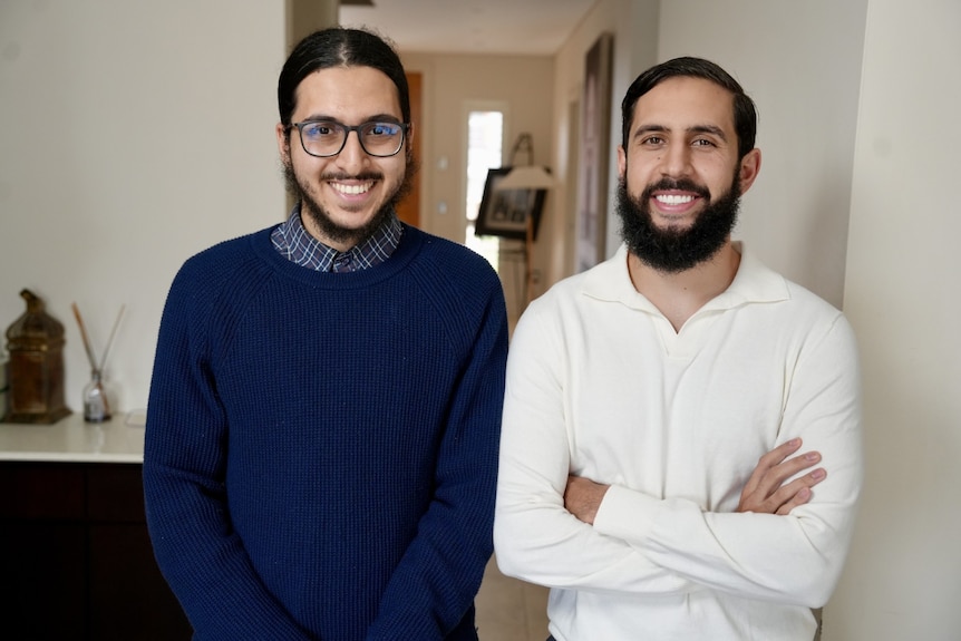 A man in a white shirt smiles with a man in a navy shirt.