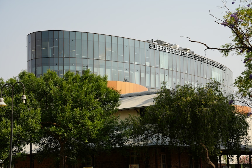 A glass window building in the distance, foreground with green trees.