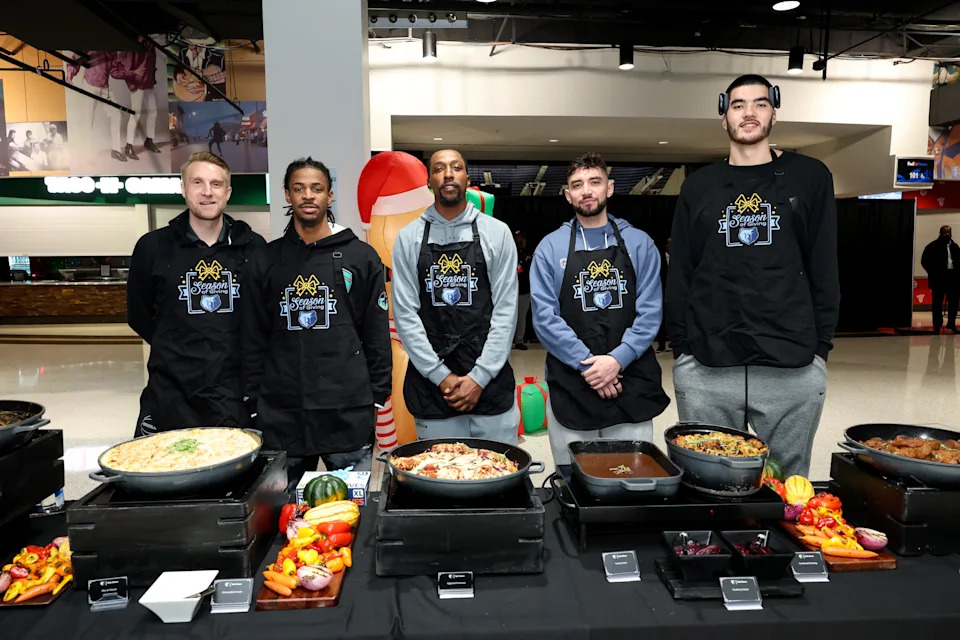 Five people in Legion aprons stand behind a table of varied dishes at a sports event venue
