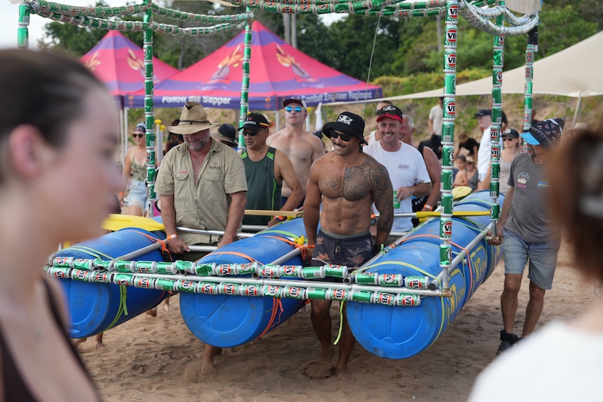 Men carry boat made of beer cans across sand