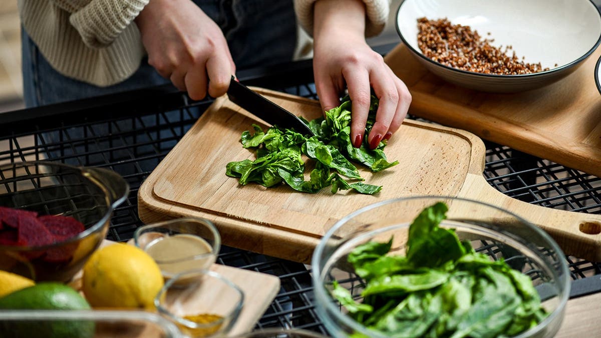 A woman chops spinach on a cutting board.