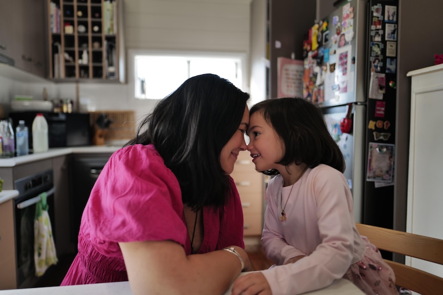 A woman and a young girl touching noses at a kitchen table.