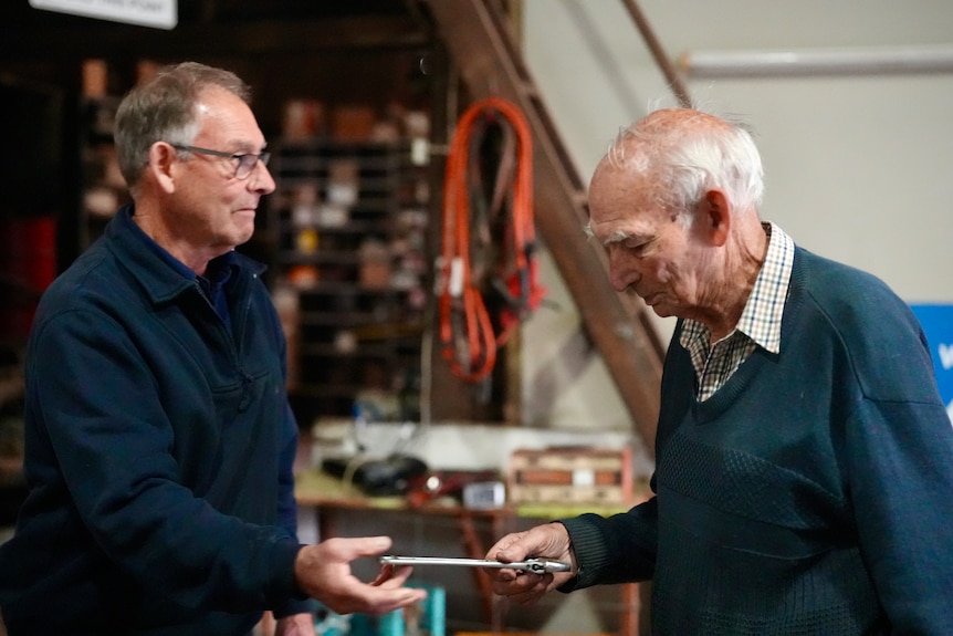 Middle aged man passing elderly father, Ray, tool in the mechanic workshop