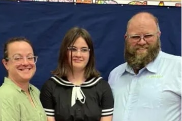 A girl stands with her family for a photo.