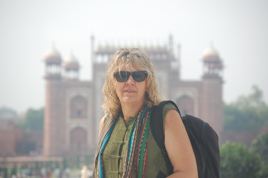 A woman with blonde hair and dark glasses in front of a large fort in India