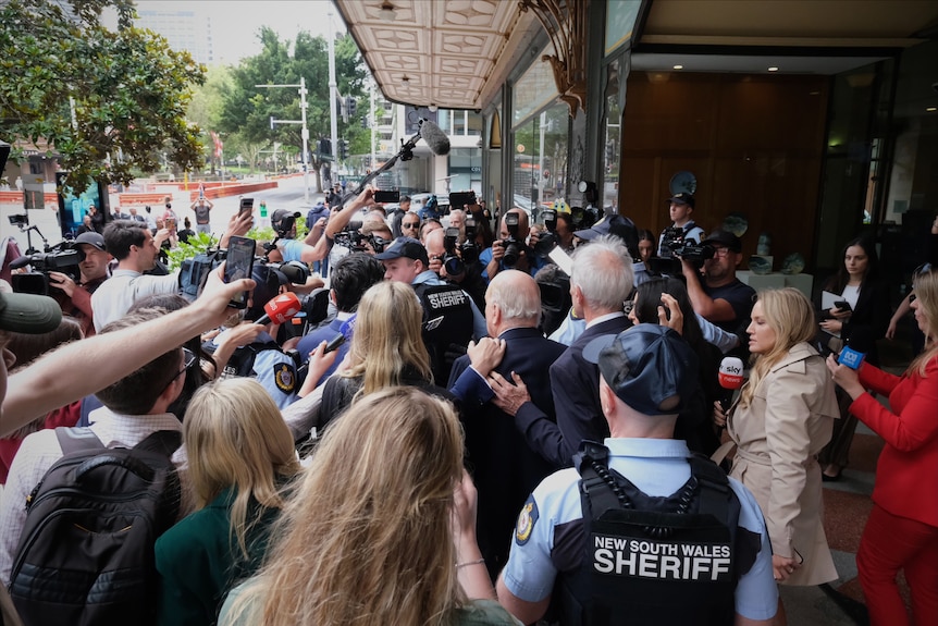 A large media scrum surrond Alan Jones outside court.