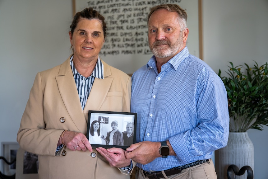 A man and woman holding a photo of their son.