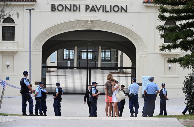 Two people embrace as police officers stand guard outside Bondi Pavilion following the attack on a Jewish holiday celebration at Sydney's Bondi Beach, in Sydney, Australia, December 15, 2025 (credit: REUTERS/Flavio Brancaleone)