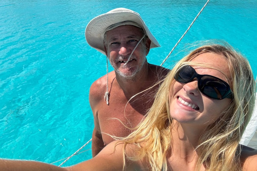 Daughter, with sunglasses and long blonde hair, her father and a bright blue sea.