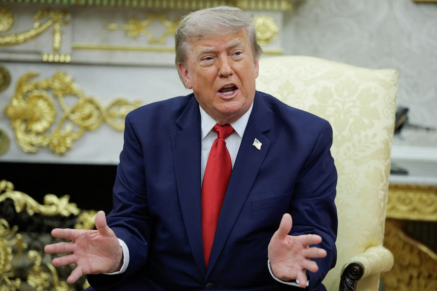 Donald Trump gestures while seated in front of the fireplace in the Oval Office.