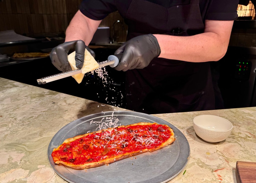 A chef shreds pecorino cheese over a crisp flatbread at Roman God of Fire.