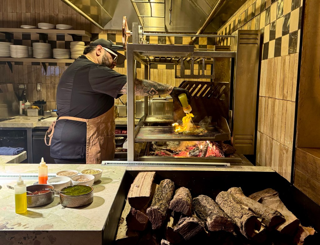 A chef squeezes oil on shrimp cooking on a grill.