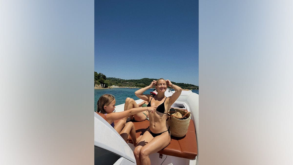 Kate Hudson sits aboard a boat while daughter Rani points toward the water during a family vacation in Greece.