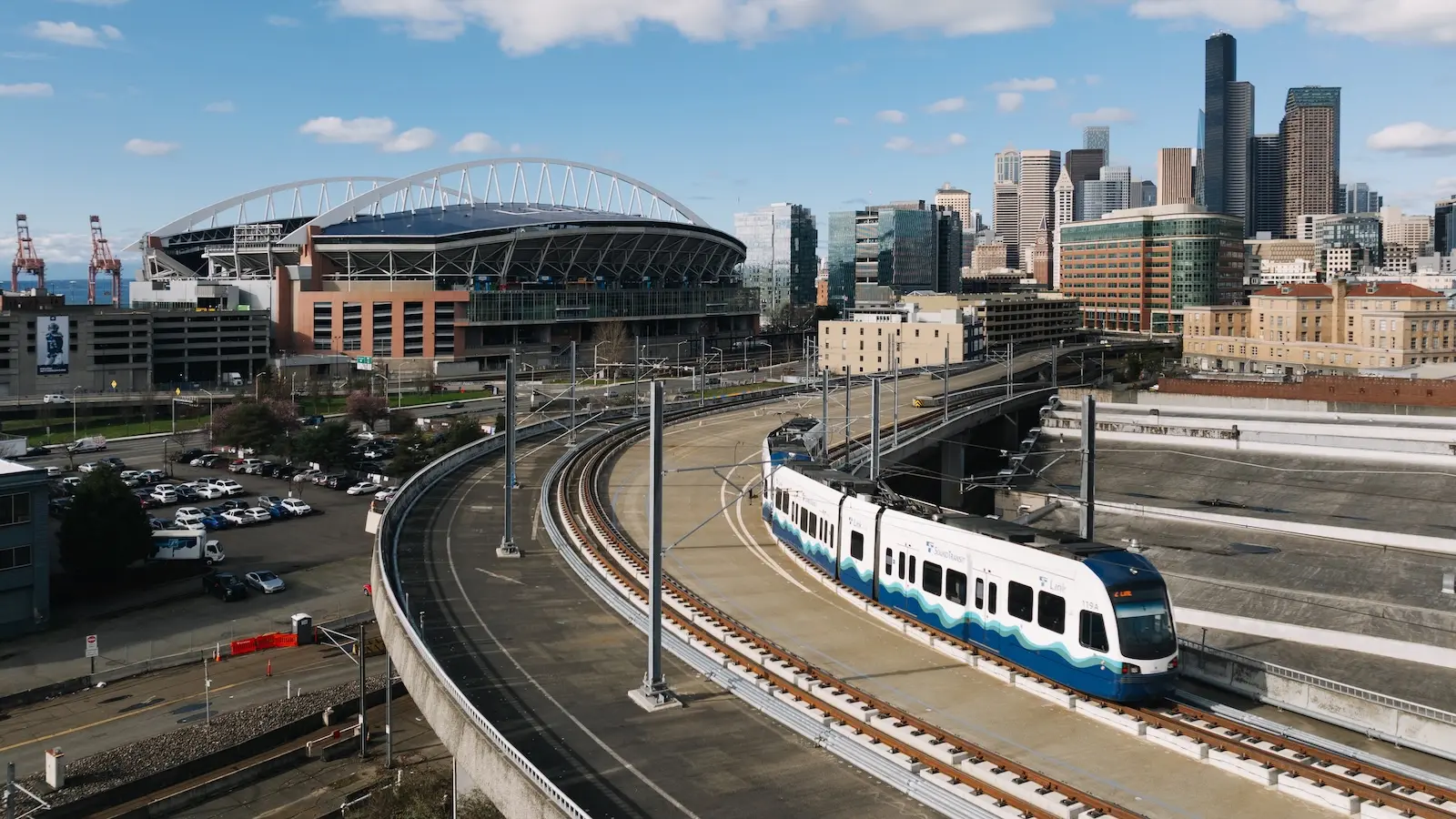 A light rail commuter train passes by Seattle Stadium on a bright sunny day