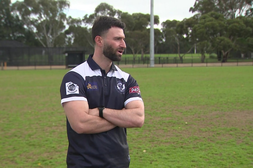 A man in an AFL jersey speaks at a football oval