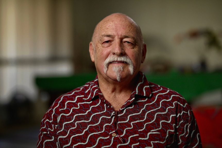 An older man with a white moustache and red top